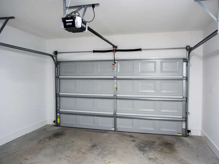 A gray garage door is open with an opener and springs visible.
